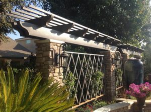 A stone wall with a metal gate and a pergola.